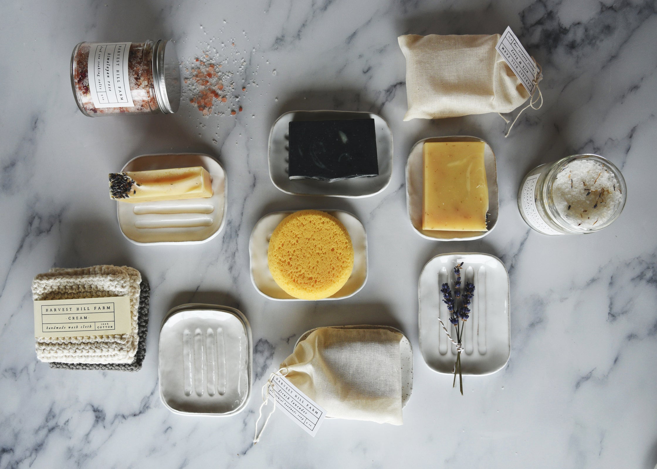 Flat lay of soaps, ceramic soap dishes and cotton cloths with botanicals on a marble background